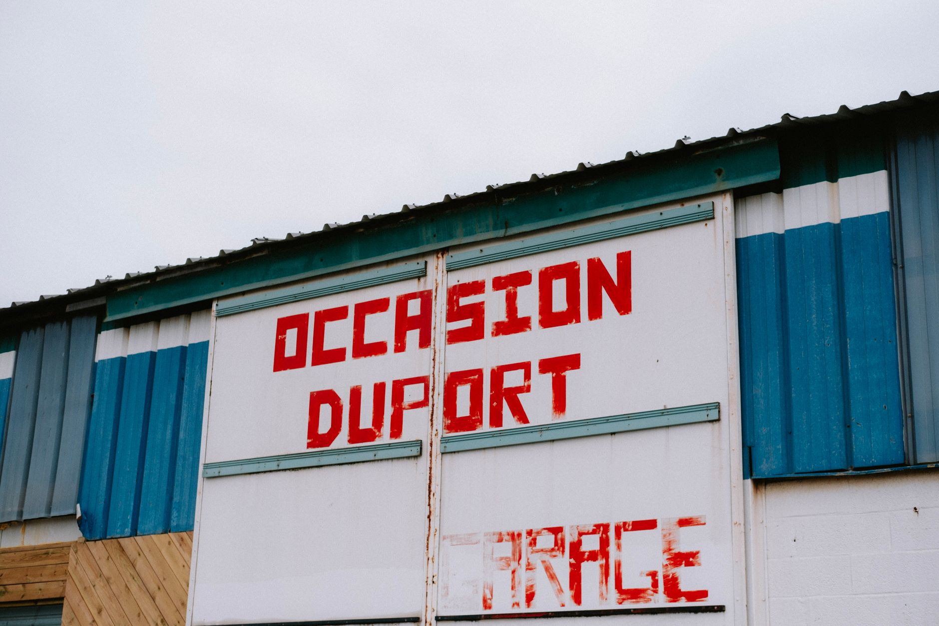 professionnel contrôlant la fixation et nettoyant une enseigne extérieure sur la façade d’une entreprise à Dunkerque